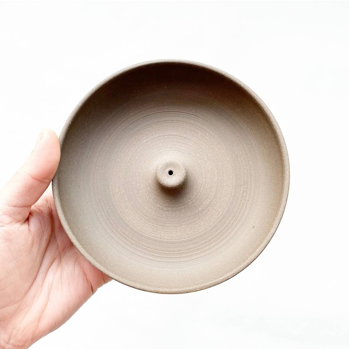 Hand holding a beige ceramic incense burner against a white background
