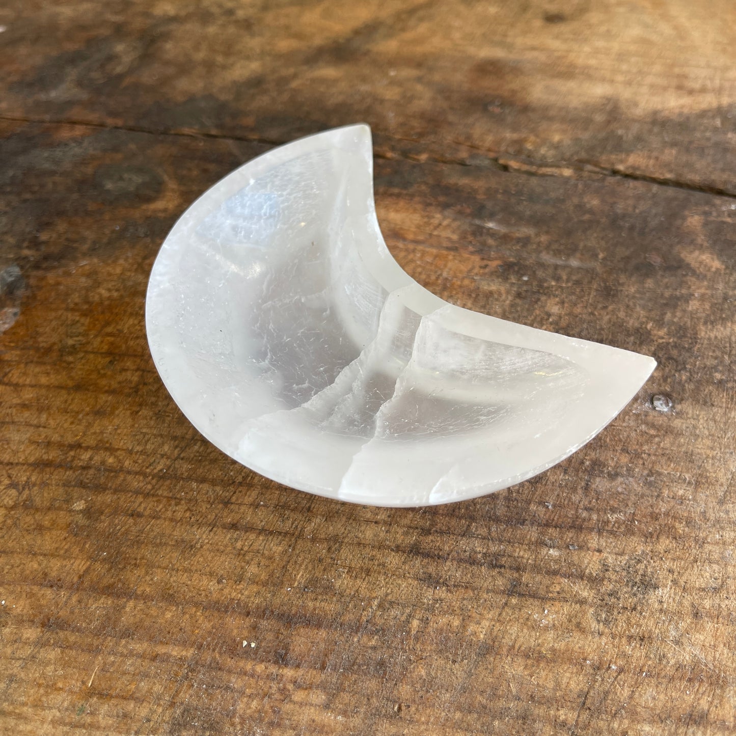 White moon shaped selenite dish on a wooden surface
