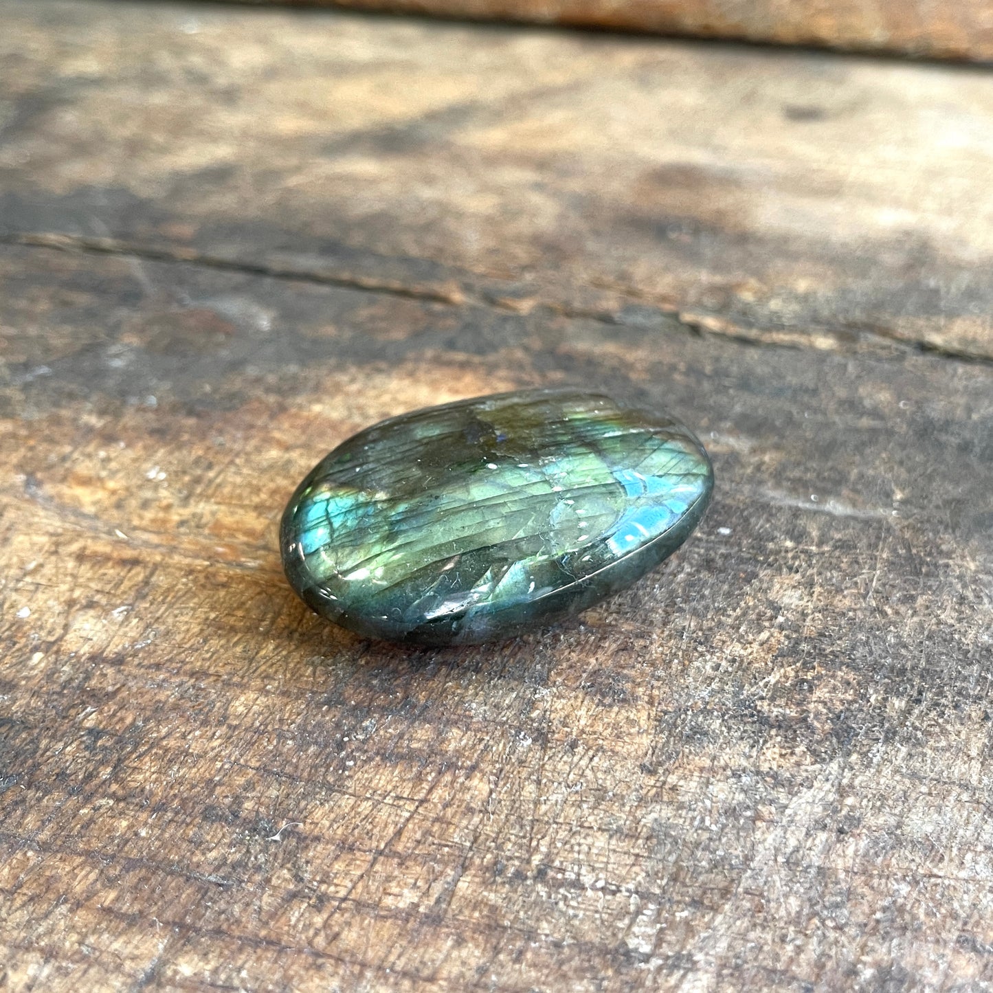 Oval-shaped gemstone with reflective surface on a wooden background