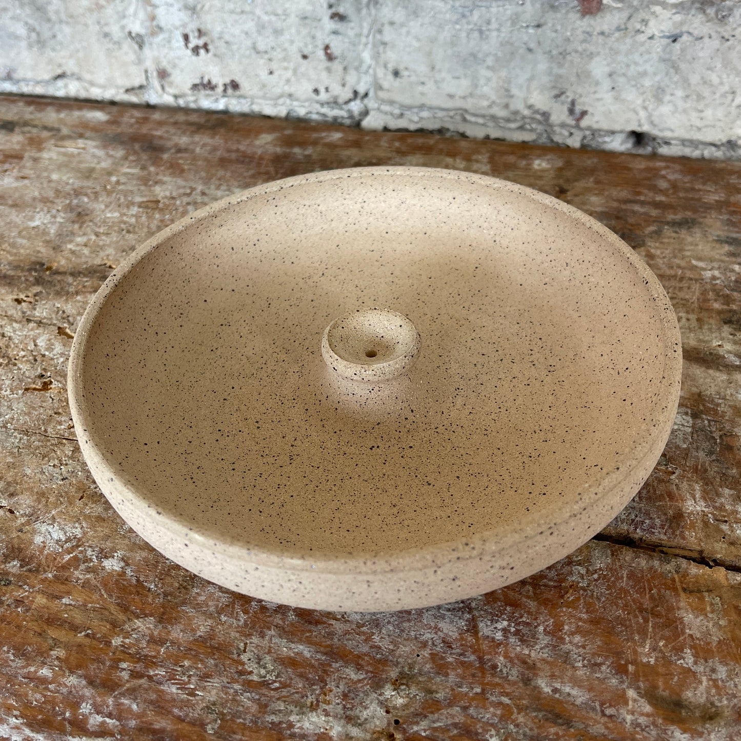 Speckled beige ceramic incense burner on a textured wooden surface