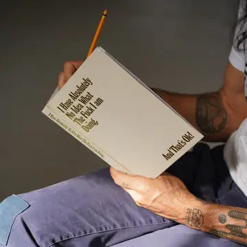 Person holding a book with text on the cover, sitting against a gray background
