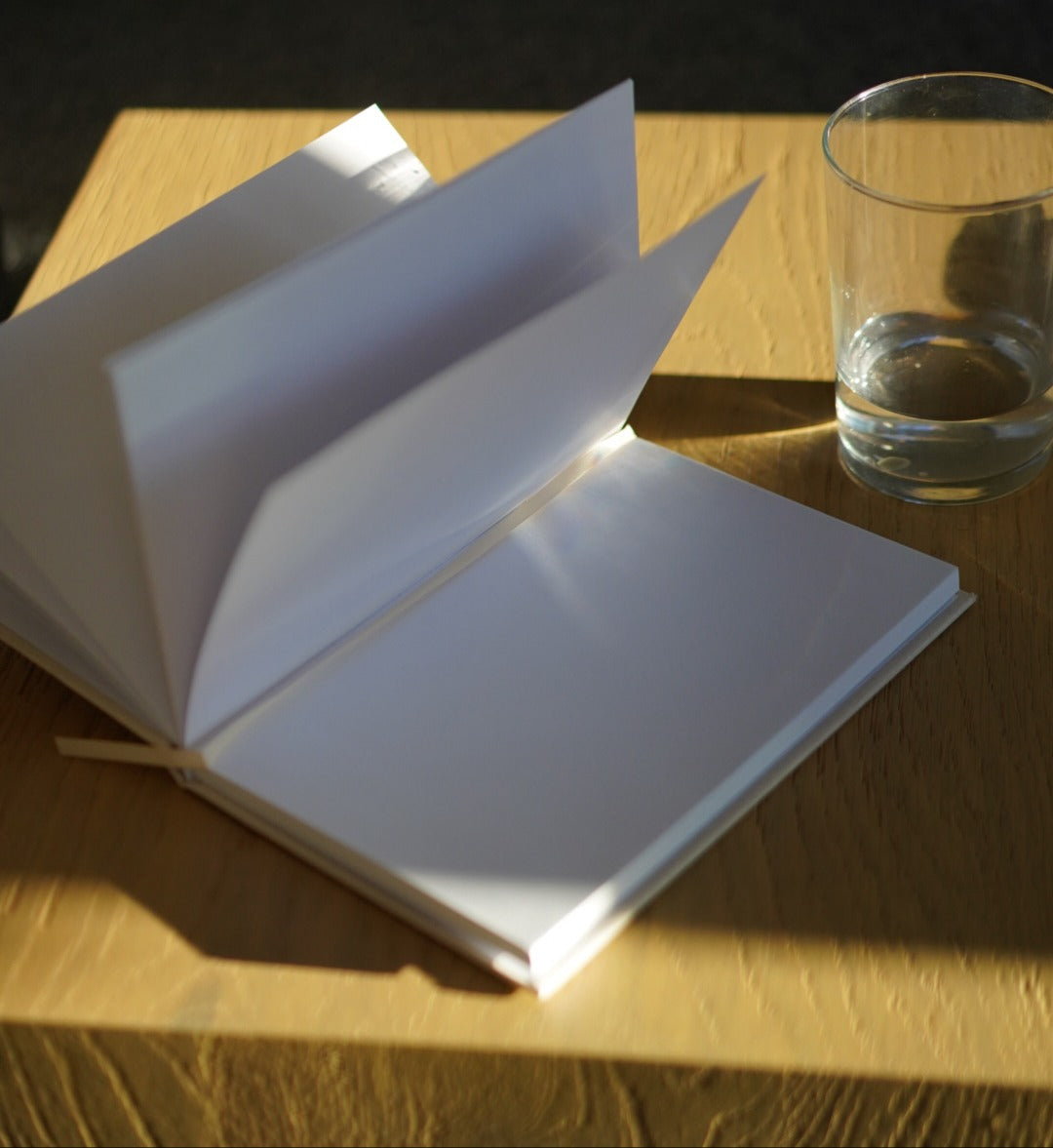 Open book on a wooden surface with a glass of water next to it