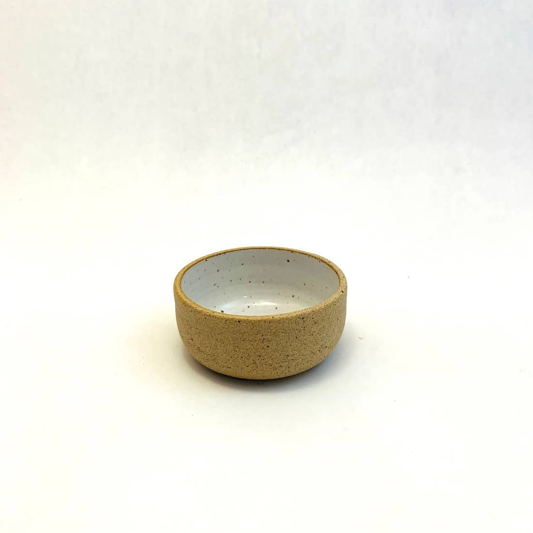 A small, beige, hand-made ceramic bowl on a white background.