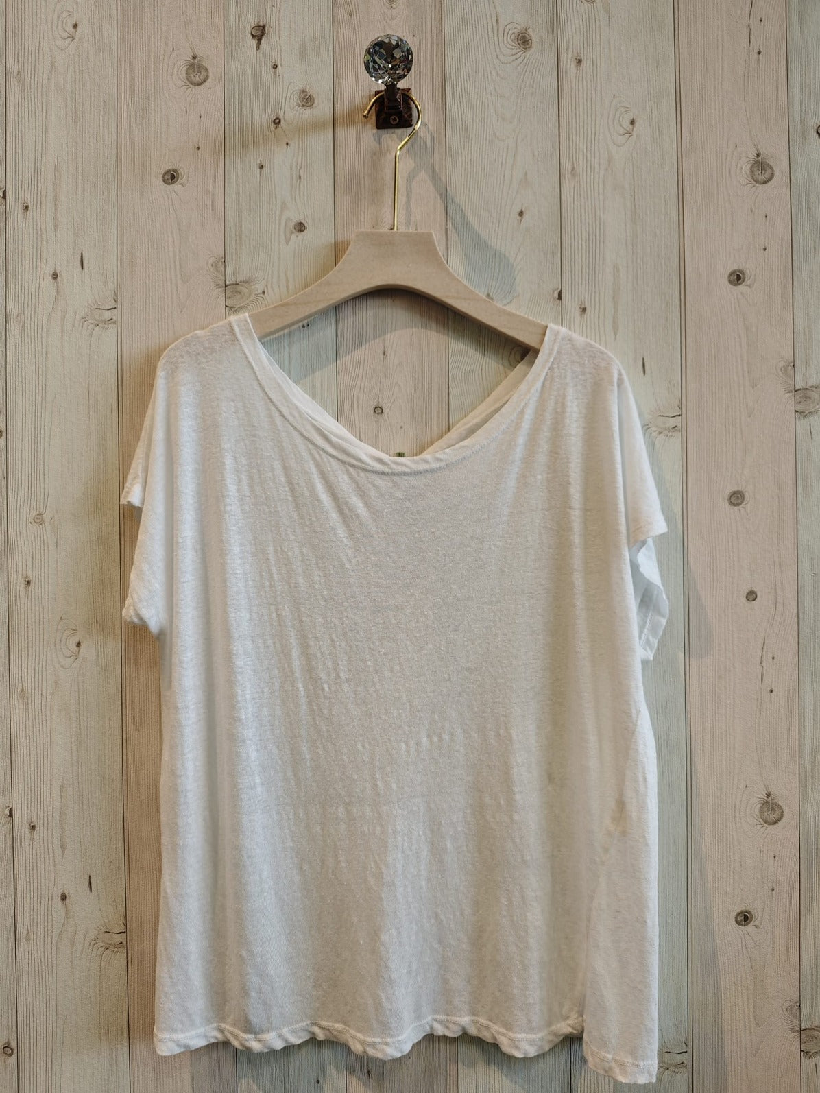 White t-shirt on a wooden hanger against a wooden wall.