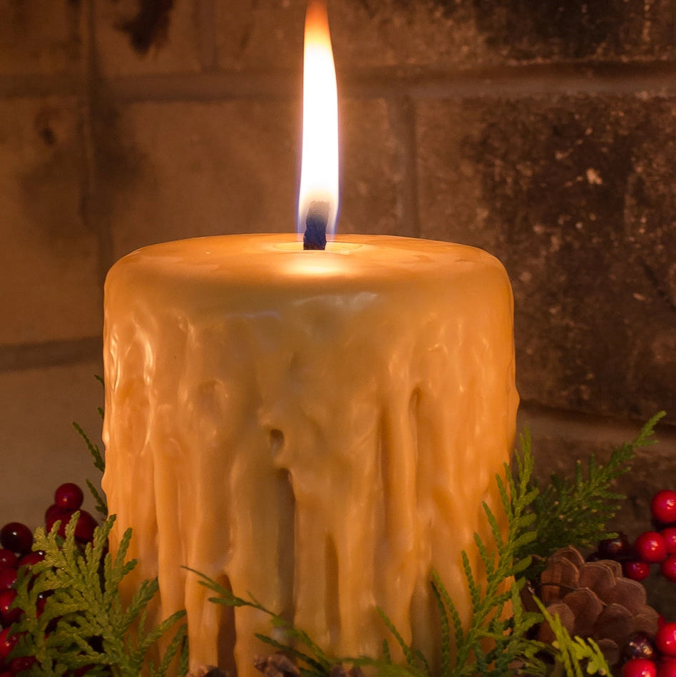 Candle with a flame surrounded by greenery and berries against a stone wall background
