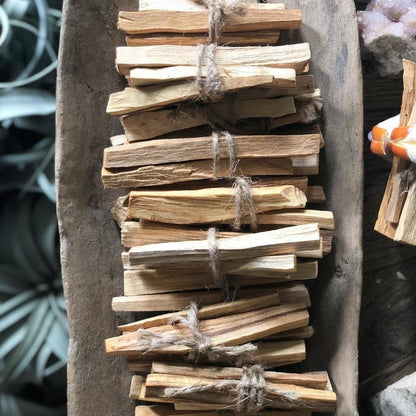 A bundle of dried palo santo sticks tied together with twine, placed upright against a wooden surface.