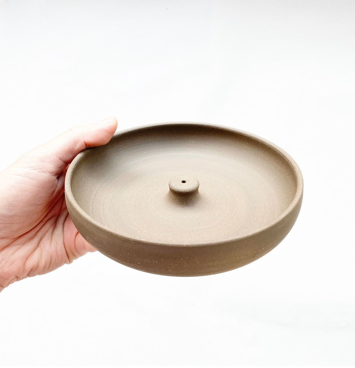 Hand holding a beige ceramic incense burner on a white background