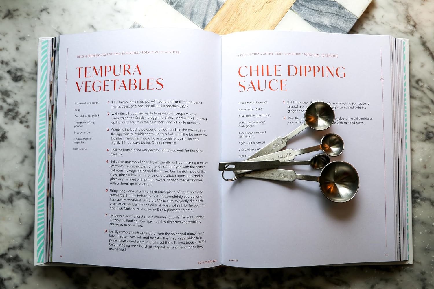 Open cookbook with recipes for tempura vegetables and chile dipping sauce, with measuring spoons on top.