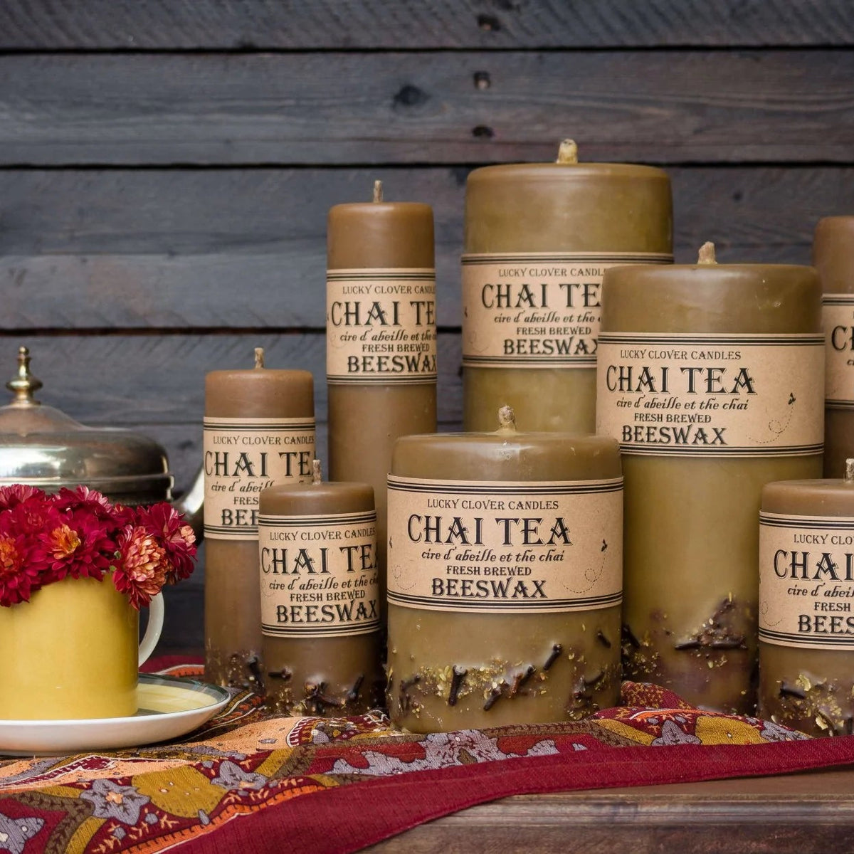 Collection of Chai Tea Beeswax candles on a wooden surface with a teapot and flowers.