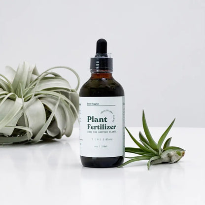 Bottle of plant fertilizer with a dropper on a white surface with plants.
