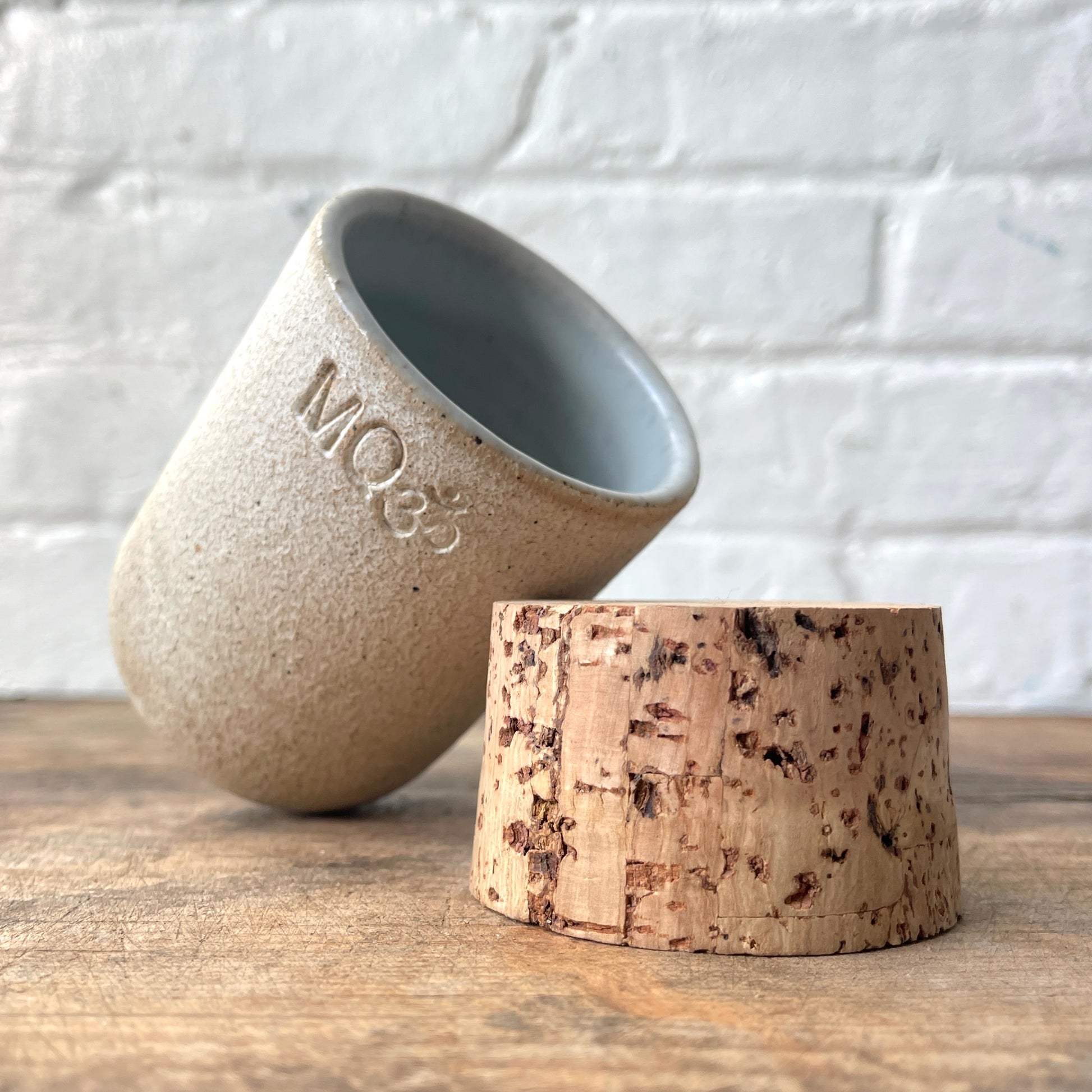 Ceramic stash with a black spiral design with a cork top, against a white brick wall.