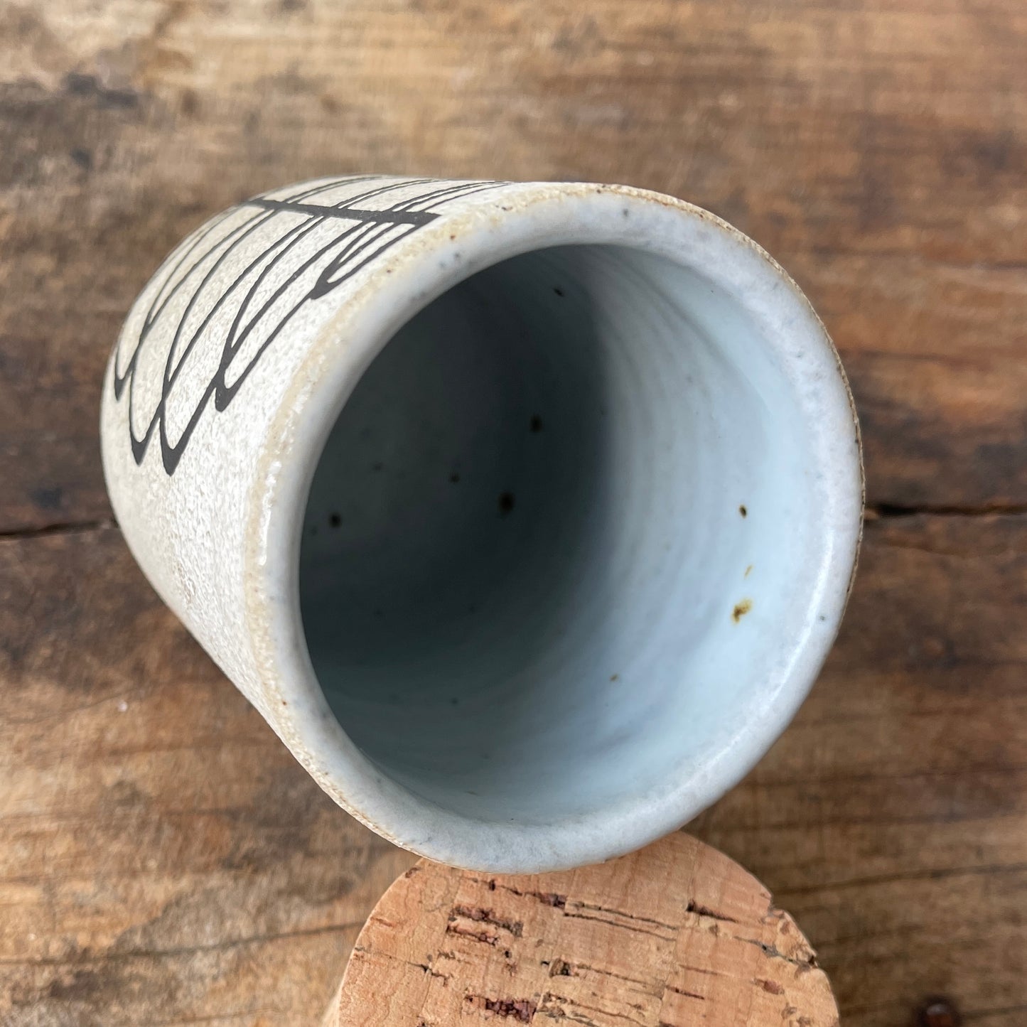 Ceramic stash with a black spiral design with a cork top on a wooden surface