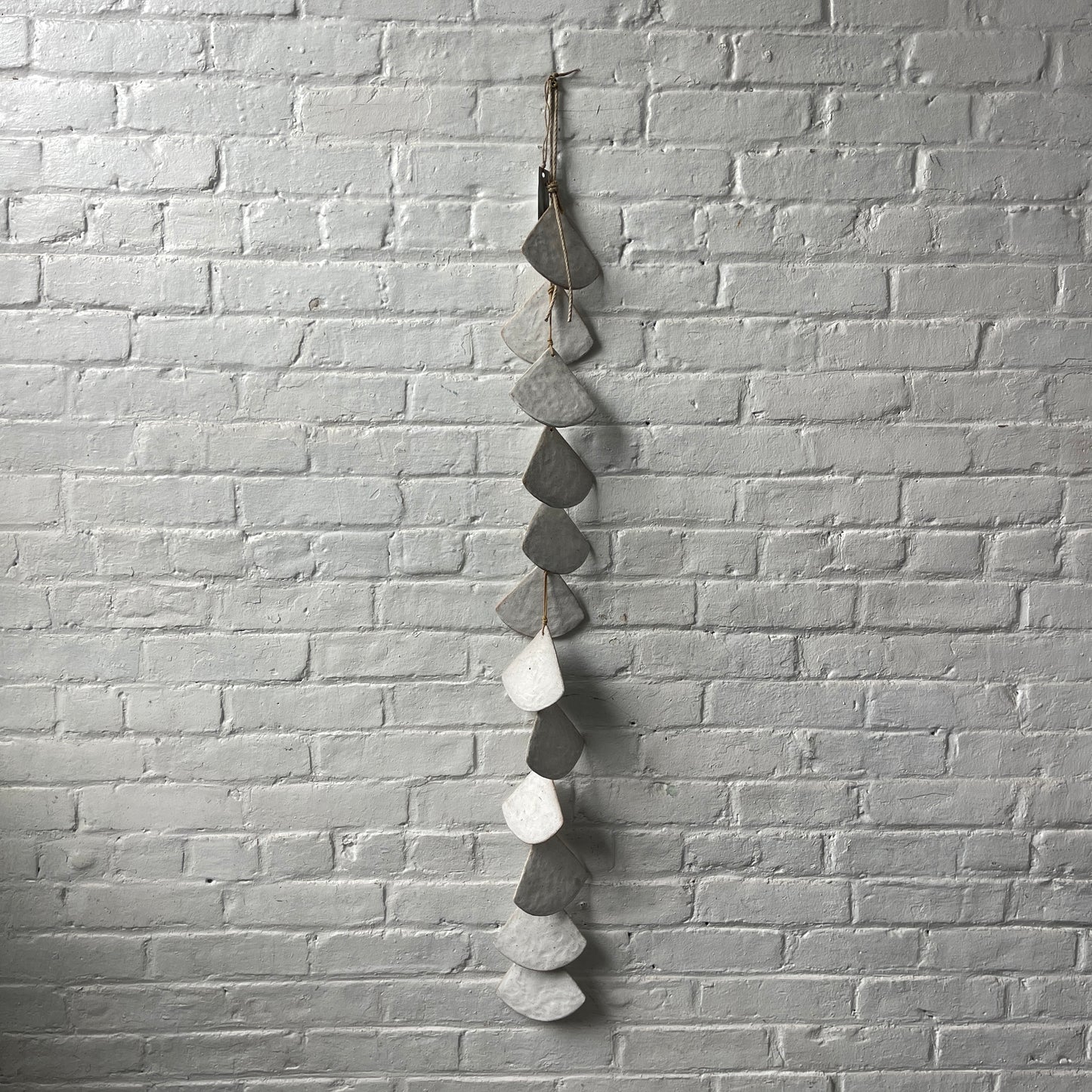 A long strand of 12 layered White stoneware shells against a white brick wall