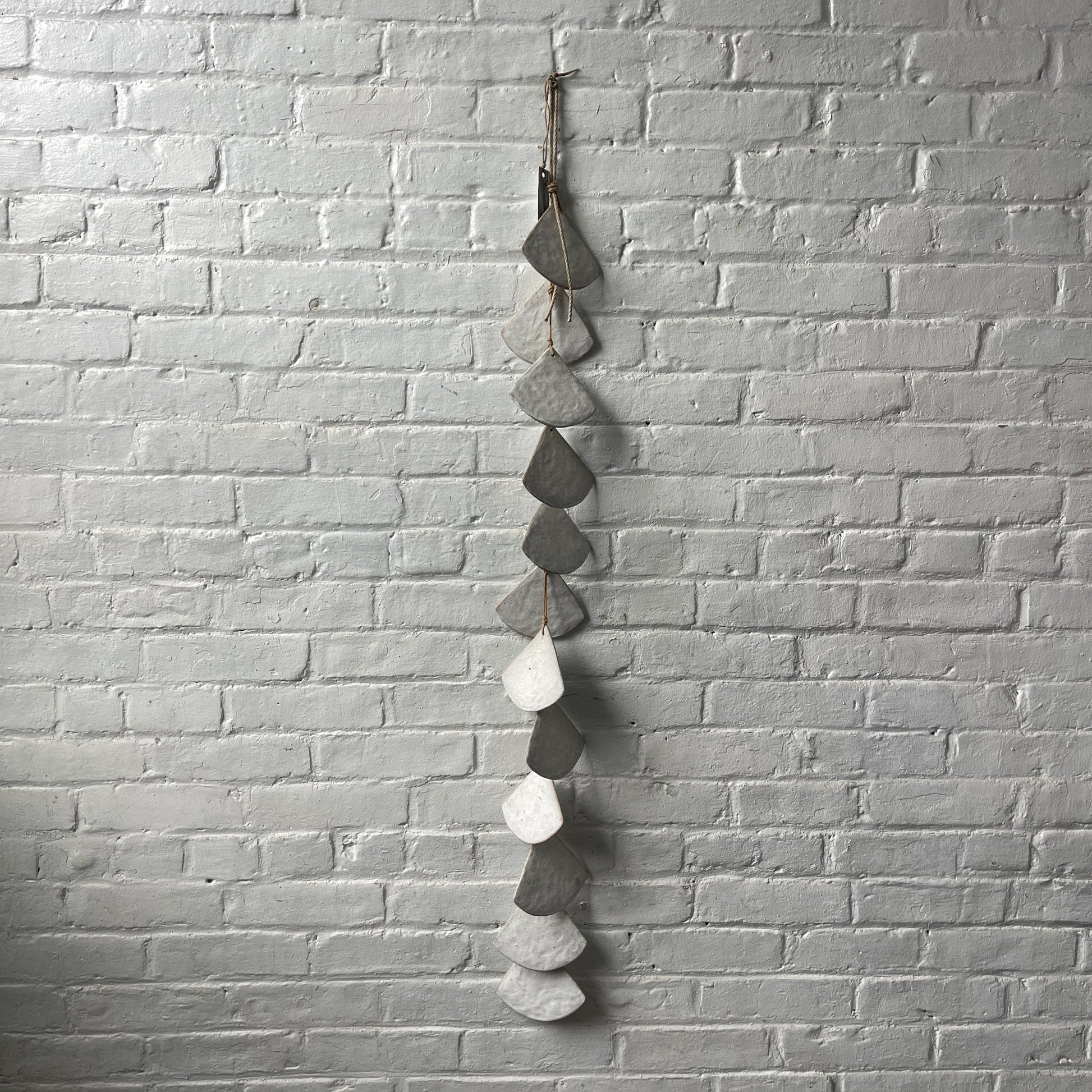A long strand of 12 layered White stoneware shells against a white brick wall