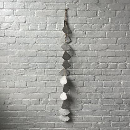 A long strand of 12 layered White stoneware shells against a white brick wall