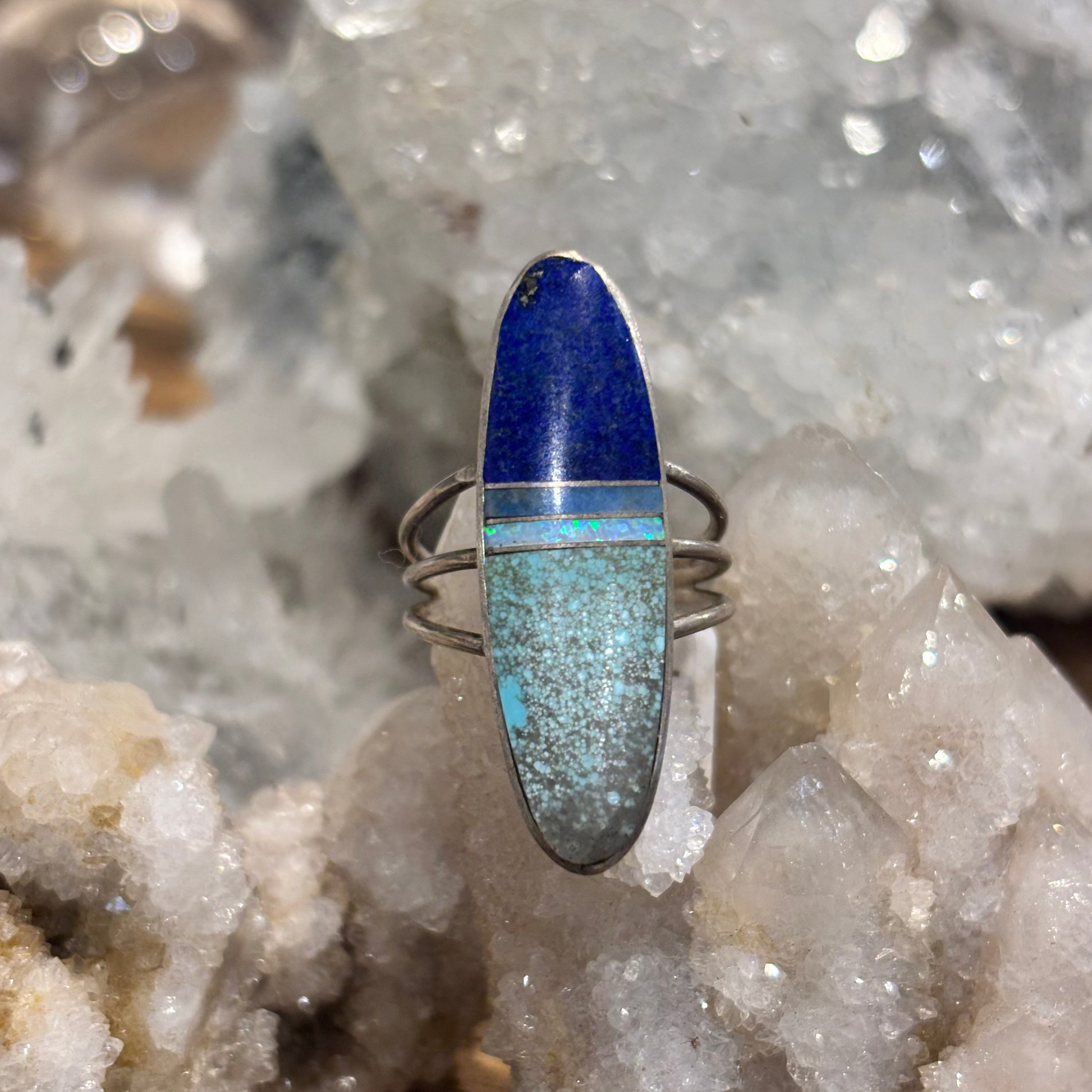 A silver ring featuring an oval inlay of lapis lazuli and turquoise, displayed on a crystal cluster.