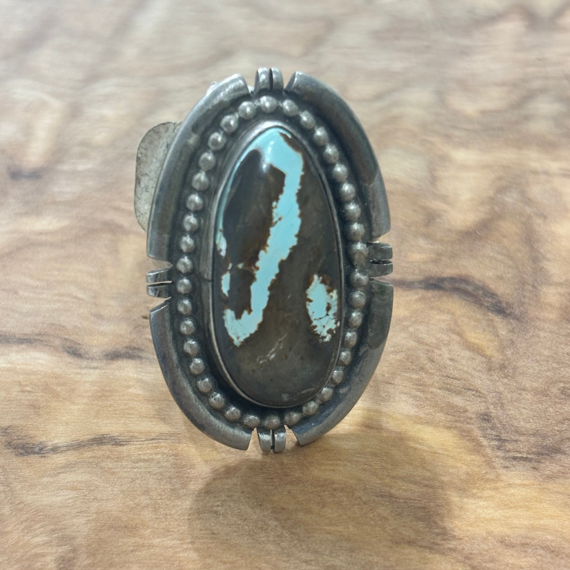 A sterling silver ring with a large oval turquoise stone featuring black and white marbling, displayed on a textured wood background.