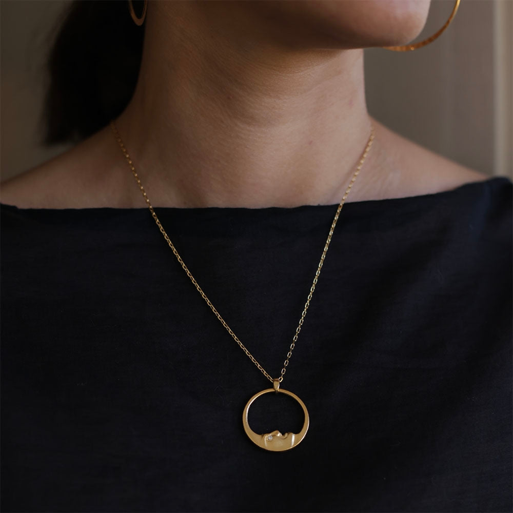 Gold necklace with a pendant worn by a person against a dark background