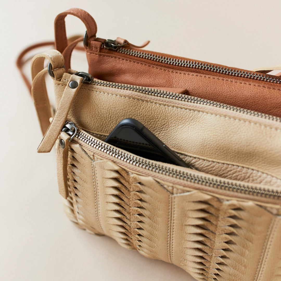 Beige leather handbag with textured surface and multiple zippers on a light background