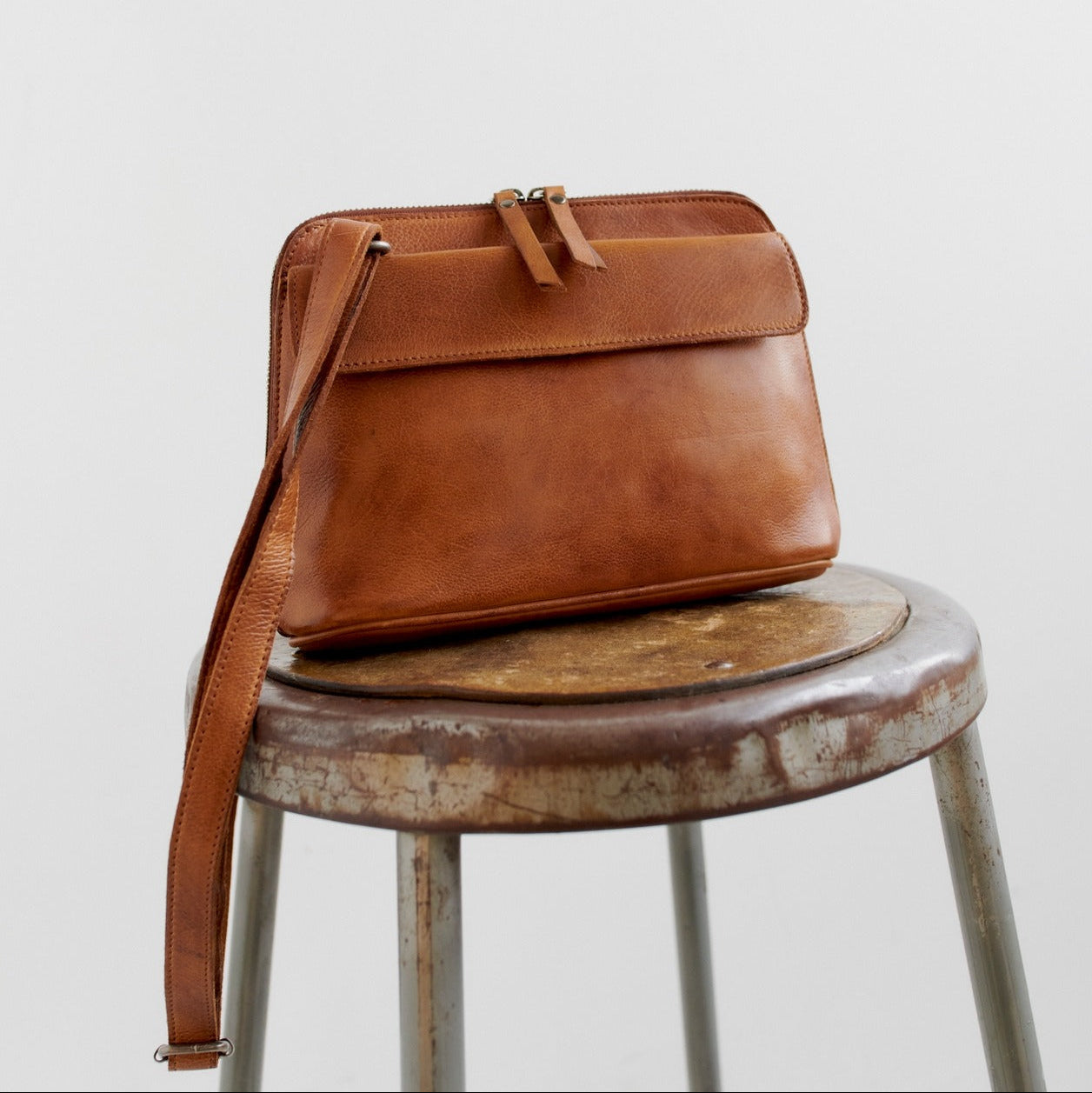Brown leather bag on a rustic stool against a light background
