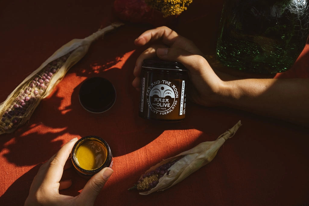 Person holding a small container of yellow powder next to a black container with text on an orange surface.