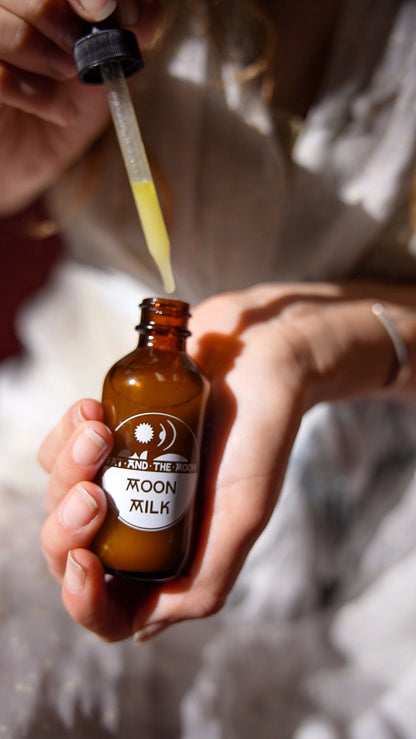 Person holding a bottle labeled 'Moon Milk' with a dropper adding liquid.