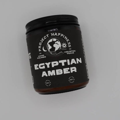 Black container labeled 'Egyptian Amber' by 'Project Happiness' on a gray background