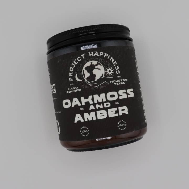Jar of 'Oakmoss and Amber' candle with 'Project Happiness' branding on a gray background