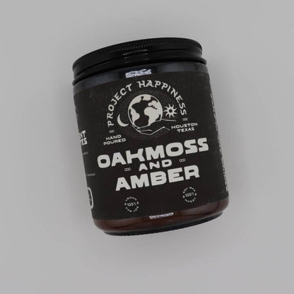 Jar of 'Oakmoss and Amber' candle with 'Project Happiness' branding on a gray background