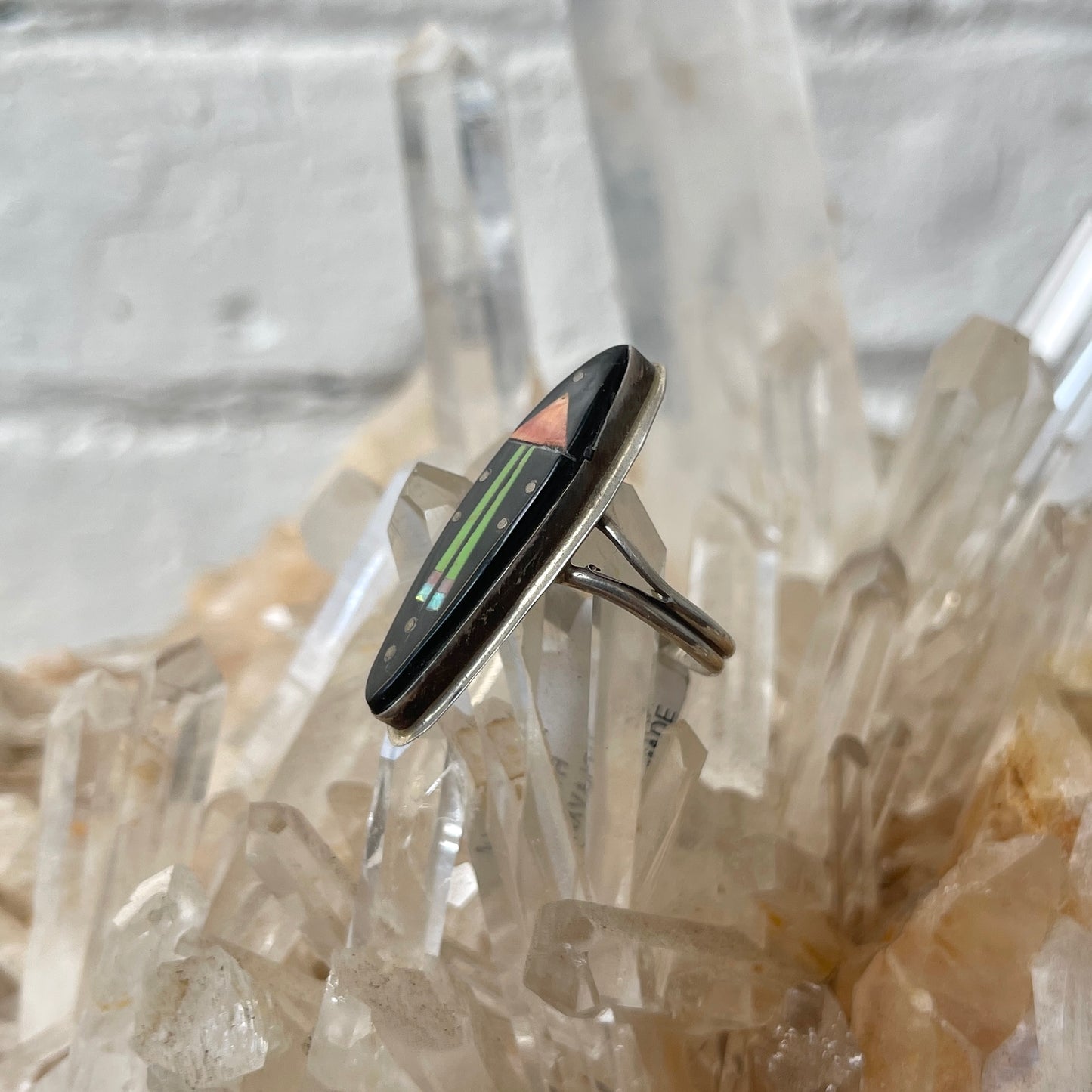 Silver ring with a black stone and colorful inlay on crystal background