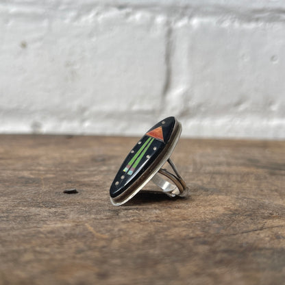 Silver ring with a black stone and colorful inlay on a wooden surface