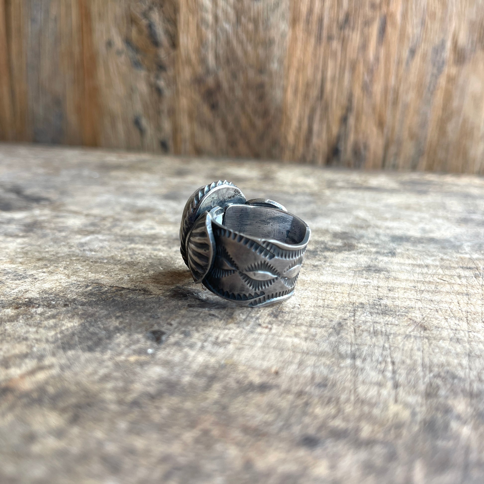 Silver ring with intricate designs on a wooden surface