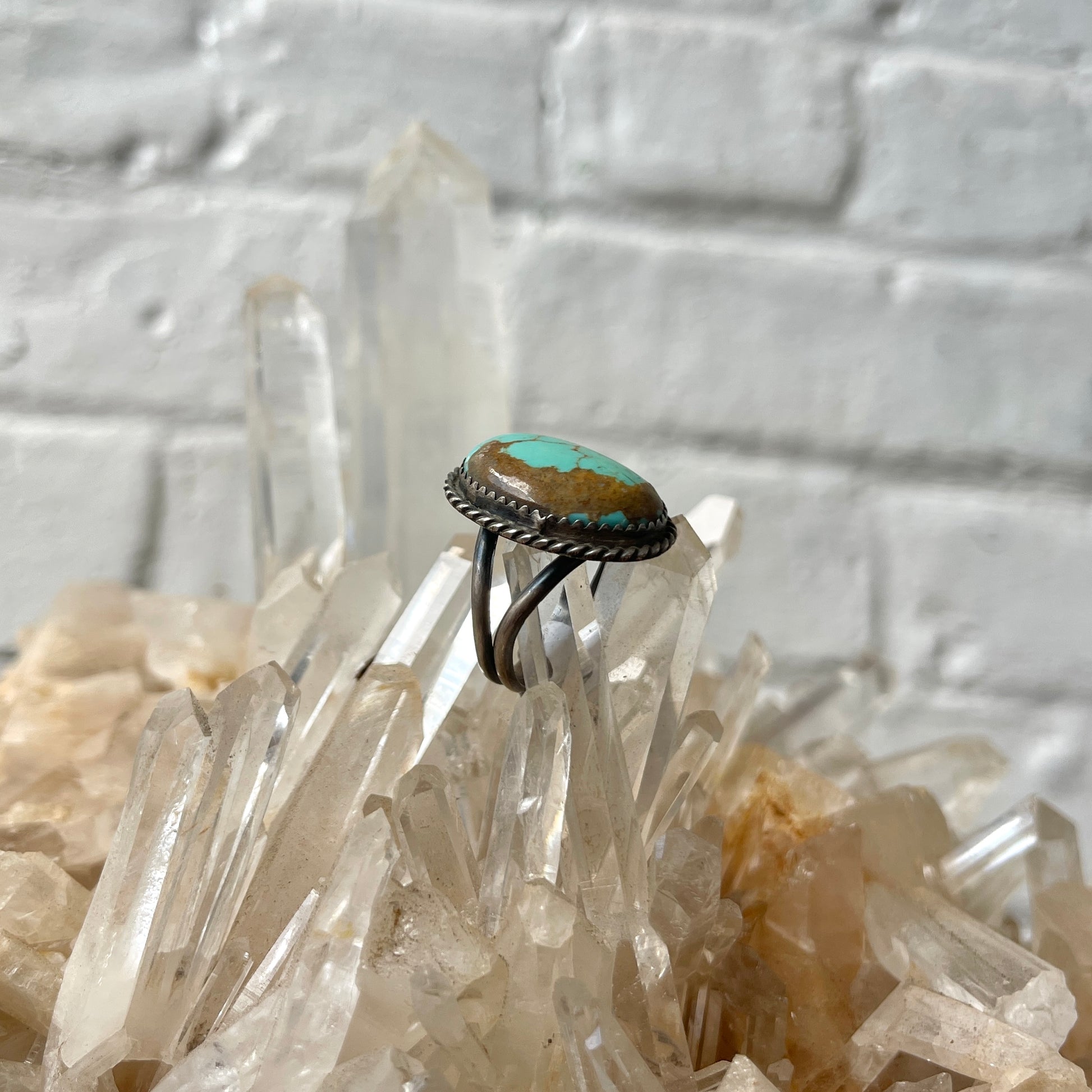 Ring with turquoise stone on a crystal formation against a textured white background