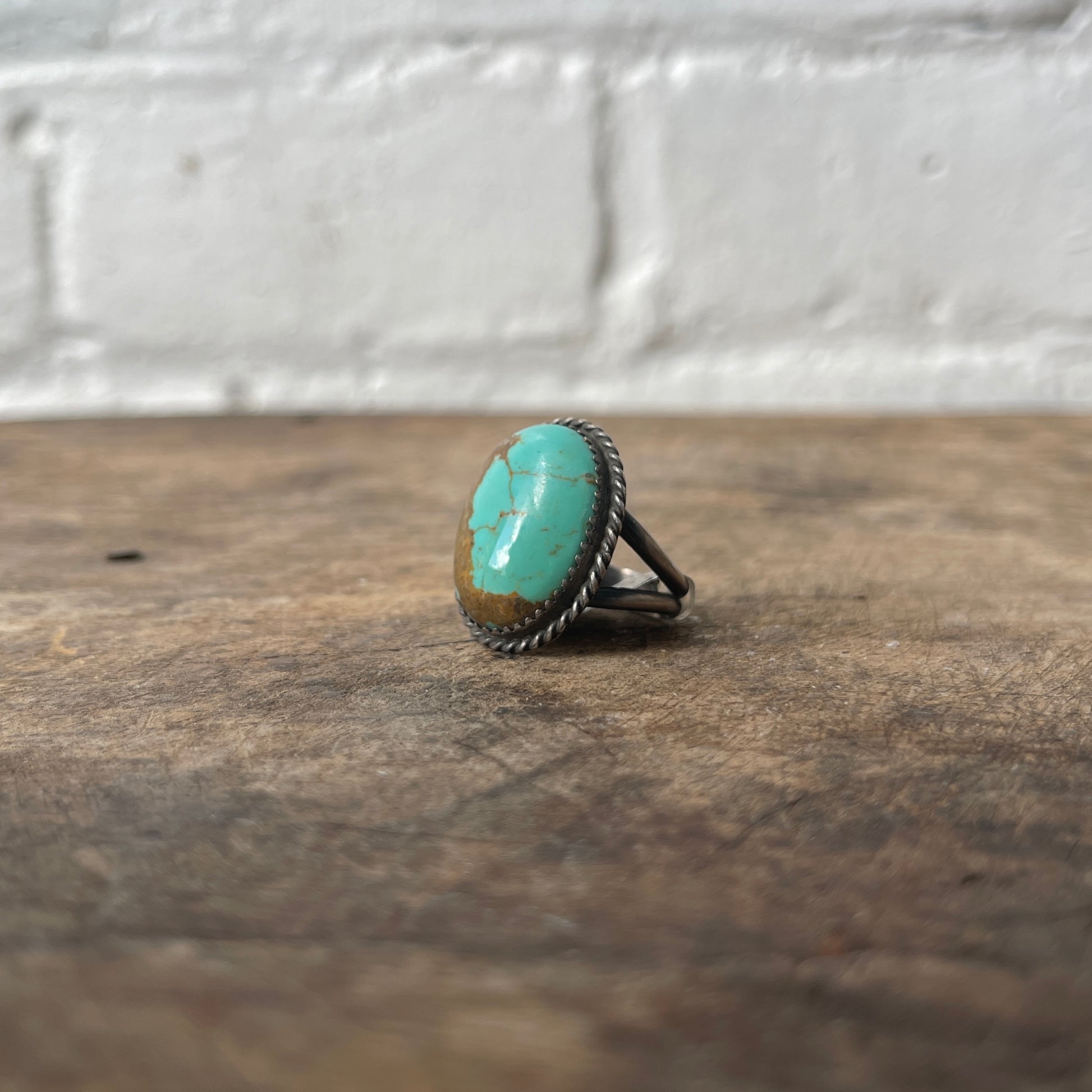 Turquoise ring on a wooden surface with a white brick wall background