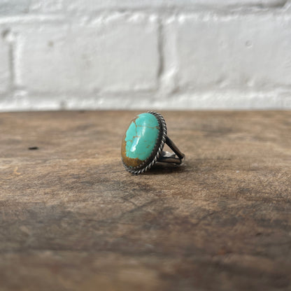 Turquoise ring on a wooden surface with a white brick wall background