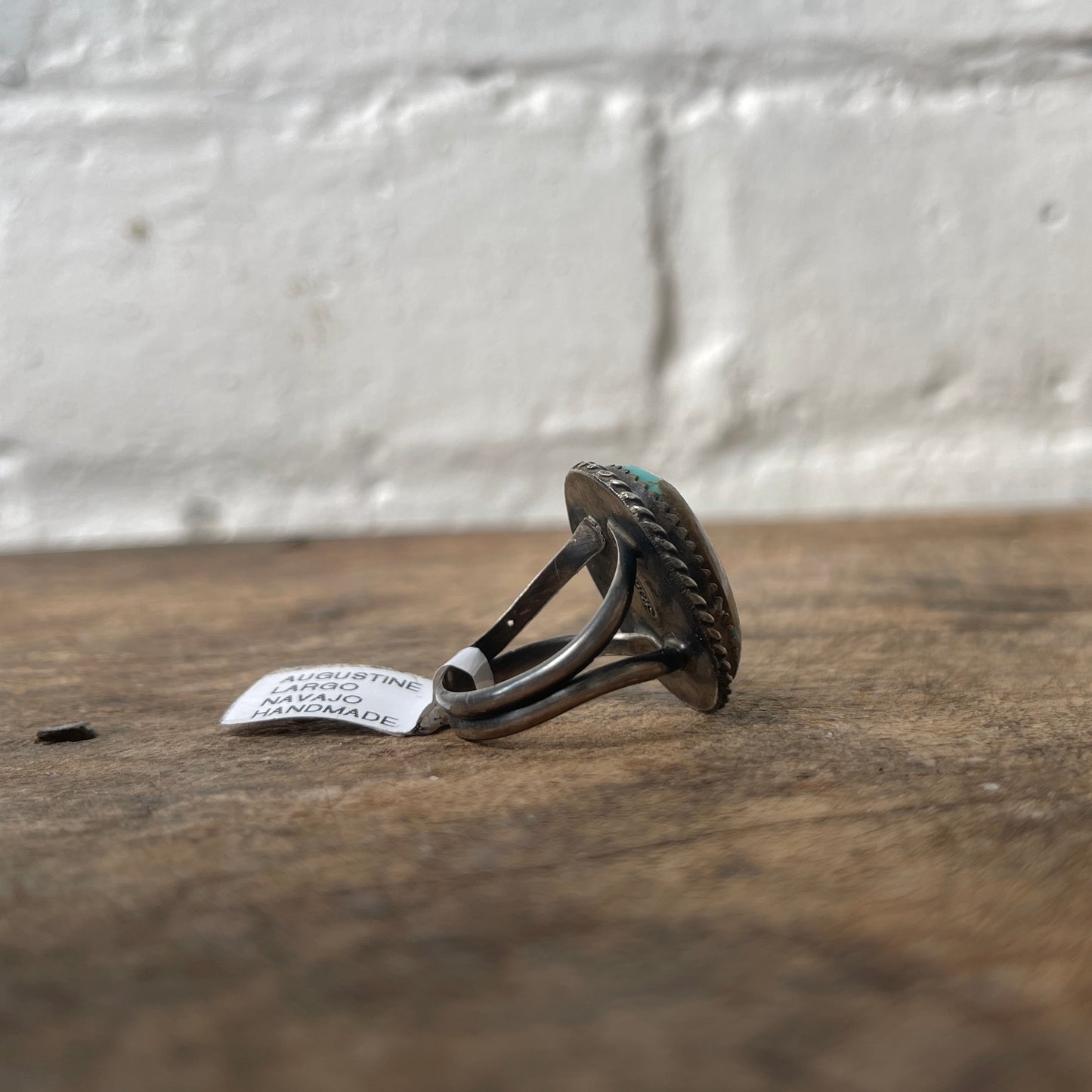 Silver ring with textured design on a wooden surface with a white label.