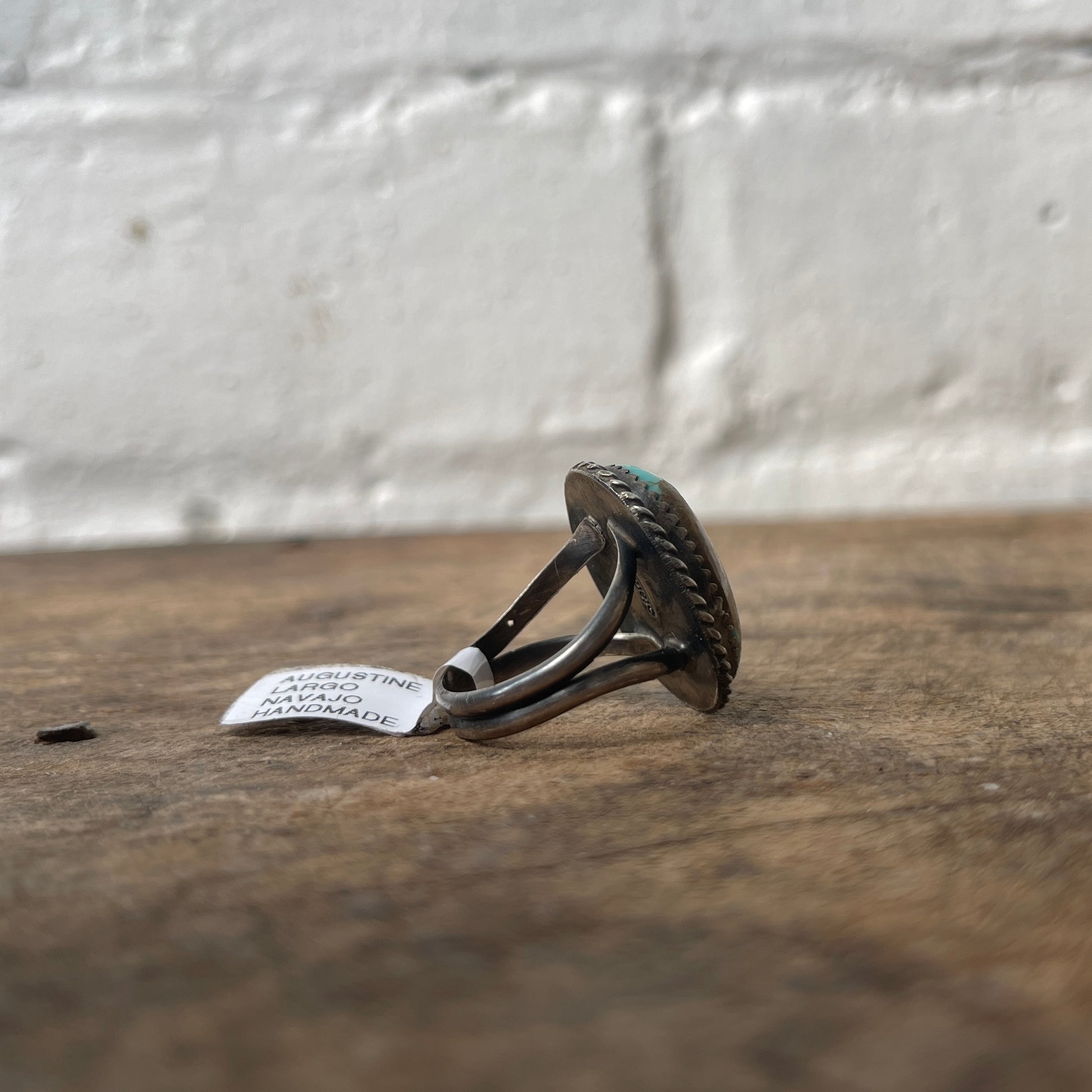 Silver ring with textured design on a wooden surface with a white label.