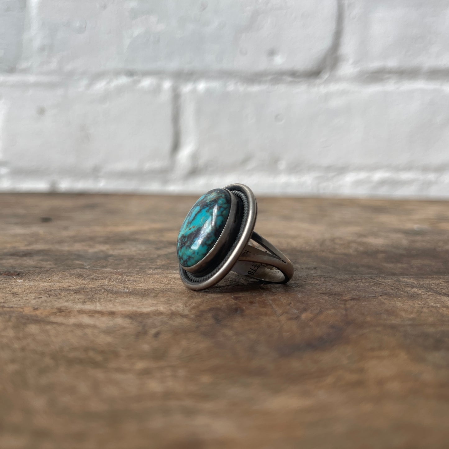 Silver ring with a turquoise stone on a wooden surface with a white brick wall background