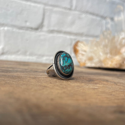 Turquoise ring on a wooden surface with a white brick wall background