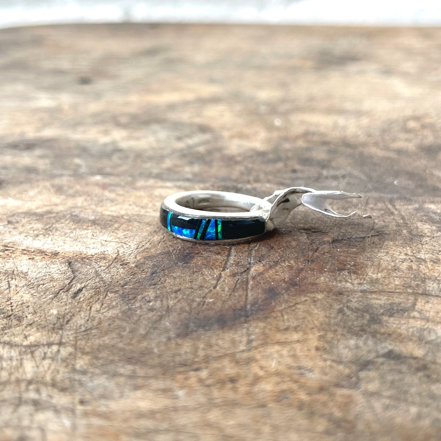 Silver ring with a colorful stone on a wooden surface