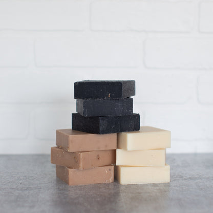 Stack of different colored soap bars on a gray surface with a white tiled wall background