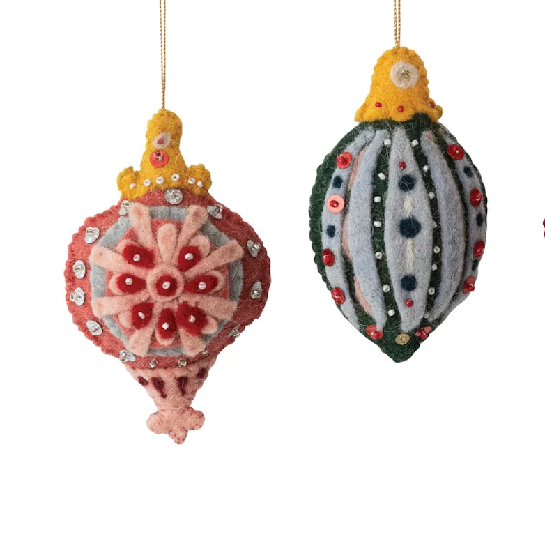 Two handcrafted felt Christmas ornaments hanging against a plain white background. One ornament is hot-air balloon-shaped in dusty red, pink, and yellow with rhinestone accents.