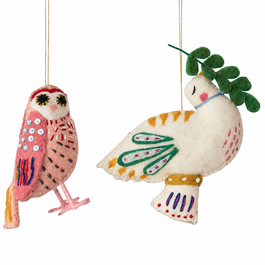 Two handmade felt Christmas ornaments shaped like an owl and a dove, hanging by thin strings against a plain white background.