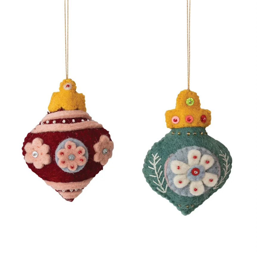 Two handmade felt Christmas ornaments hanging against a white background. One ornament is deep red with pink and light blue floral details and a yellow top.