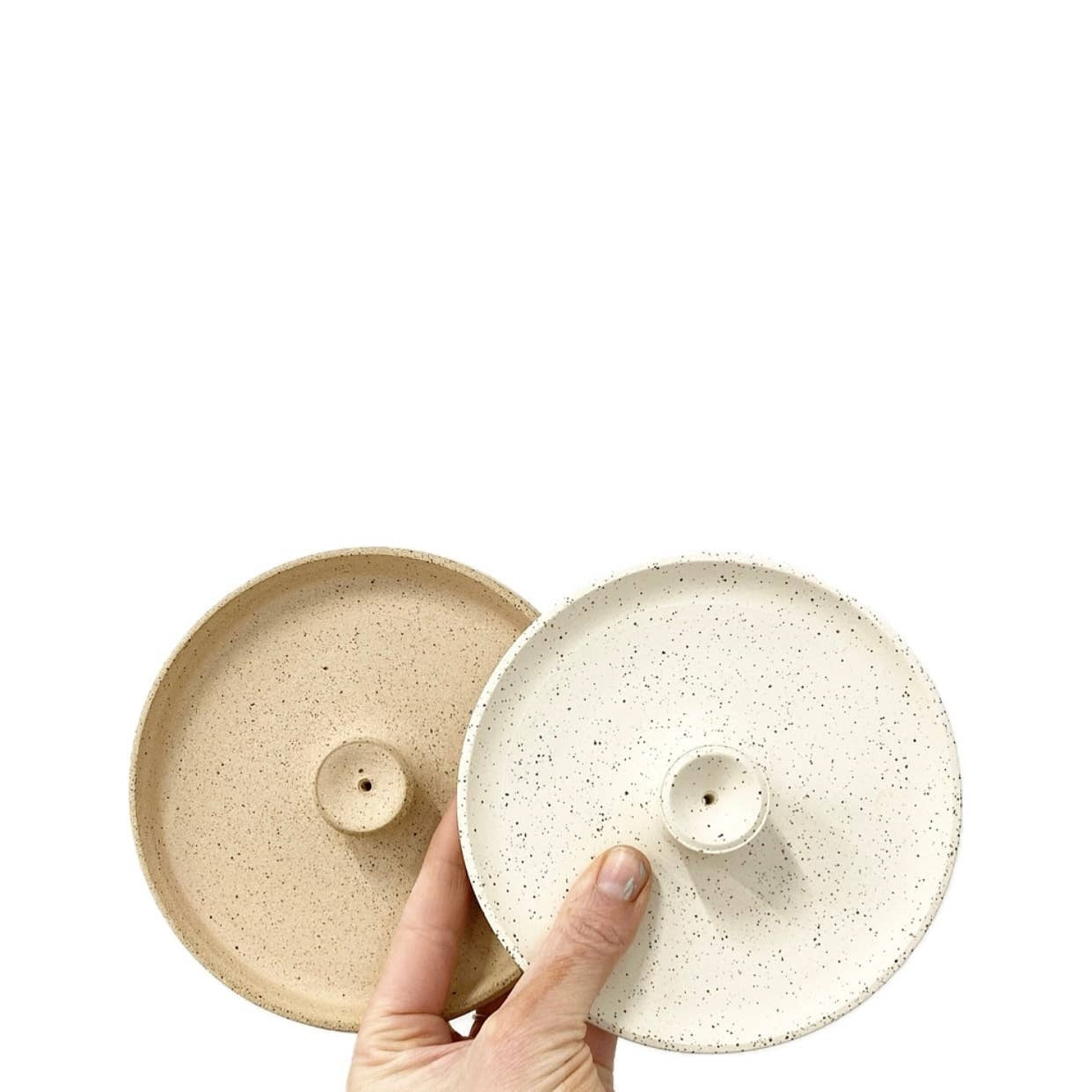 Hand holding two ceramic incense holders with a speckled finish on a white background