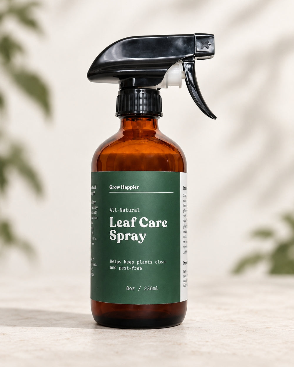 An amber glass spray bottle of Grow Hopsler All-Natural Leaf Care Spray with a dark green label and black trigger sprayer, set on a light stone surface with soft leaf shadows in the background.
