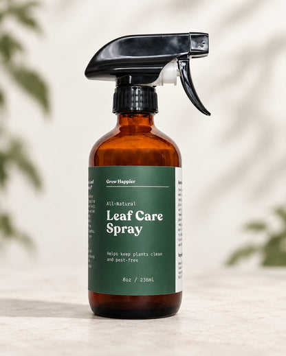 An amber glass spray bottle of Grow Hopsler All-Natural Leaf Care Spray with a dark green label and black trigger sprayer, set on a light stone surface with soft leaf shadows in the background.