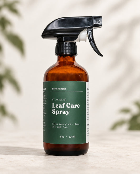 An amber glass spray bottle of Grow Hopsler All-Natural Leaf Care Spray with a dark green label and black trigger sprayer, set on a light stone surface with soft leaf shadows in the background.
