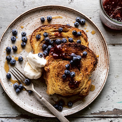 French toast with blueberries, whipped cream, and syrup on a speckled plate.