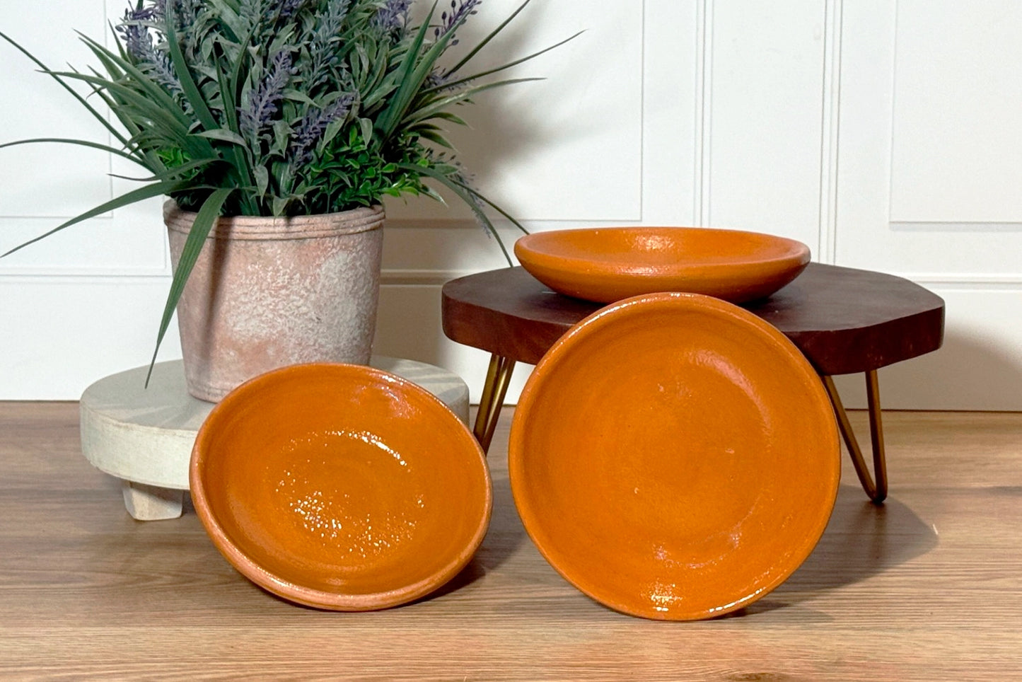 Three terracotta bowls on a wooden surface with a plant in the background.